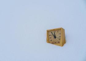 Old mechanical alarm clock in a snowdrift. Countdown to midnight. Christmas and New Years start concept. Copy space. photo