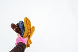 Hand holds several pairs of knitted warm mittens of different colors, against a background of white snow. Copy space. photo
