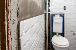 White tiles are glued to a special mortar, in the bathroom, against the background of the toilet bowl. Wall decoration process. Home repairs. photo