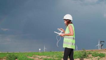 professionell ekologi ingenjör i enhetlig och hjälm innehav avlägsen kontrollant för flygande Drönare arbetssätt på vind turbin på skön solnedgång bakgrund. alternativ till elektrisk energi. video