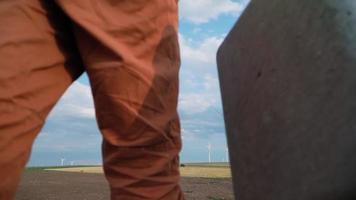 professioneel ecologie ingenieur in uniform en helm met speciaal uitrusting in hand- gaat naar onderhoud een windmolen Aan mooi lucht achtergrond. alternatief energie en wind macht fabriek. langzaam beweging. video