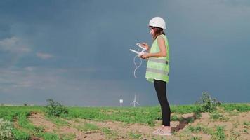 ingénieur professionnel en écologie en uniforme et casque tenant une télécommande pour voler un drone travaillant à l'éolienne sur fond de coucher de soleil magnifique. alternative à l'énergie électrique.