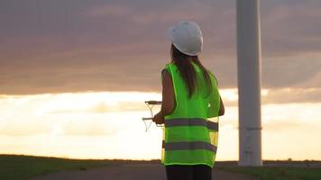 professionell ekologi ingenjör i enhetlig och hjälm innehav avlägsen kontrollant för flygande Drönare arbetssätt på vind turbin på skön solnedgång bakgrund. alternativ till elektrisk energi. video