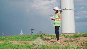 professionell ekologi ingenjör i enhetlig och hjälm innehav avlägsen kontrollant för flygande Drönare arbetssätt på vind turbin på bakgrund skön himmel regnbåge. alternativ elektrisk energi. video