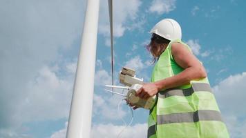 ingénieur professionnel en écologie en uniforme et casque tenant une télécommande pour voler un drone travaillant sur fond de moulins à vent. service de parc éolien. alternative à l'énergie électrique.