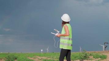 professionale ecologia ingegnere nel uniforme e casco Tenere a distanza controllore per volante fuco Lavorando a vento turbina su bellissimo tramonto sfondo. alternativa per elettrico energia. video