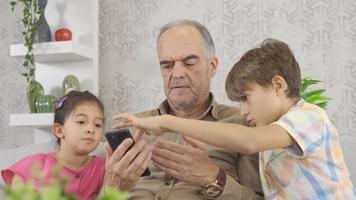 Old man is learning to use smartphone for kids. The grandchildren of the old man whose old phone broke down are teaching smartphones. video