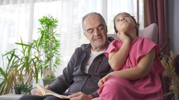 Grandpa reading a book to his grandson. Grandfather reads a book to his grandson and the grandson listens carefully. video