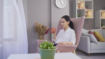 Happy woman drinking coffee by the window. Young woman sitting on a sofa and drinking her coffee. video