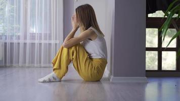 mujer deprimida llorando en el suelo. la mujer sentada en el suelo, apoyando la espalda contra la pared, está deprimida y triste. video