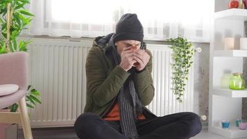 um homem frio em um apartamento frio. homem com roupas grossas sente frio em casa e se apóia na caldeira combinada. video