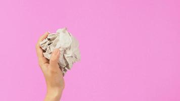 Papel arrugado. está mutilado en la mano de una mujer sobre fondo rosa.vista lateral foto