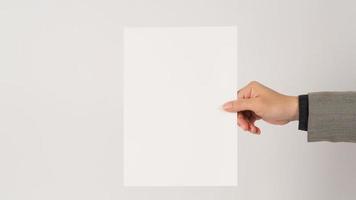 Space for text. The hand is wearing a gray suit and holding blank board A4 paper on white background. photo