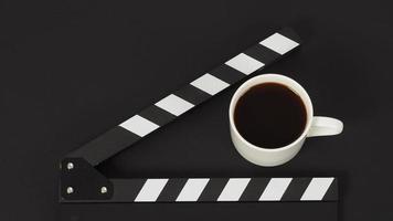 Black Clapperboard and cup of coffee on black background photo