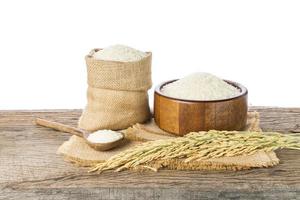 arroz blanco orgánico o arroz jazmín en un bol de madera y sacos con orejas de arroz sobre un suelo de madera sobre un fondo blanco foto