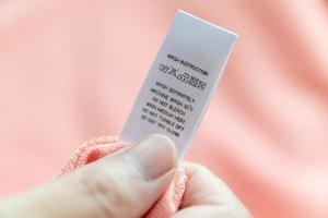 Hand hold and reading at white laundry care washing instructions clothes label on pink shirt photo