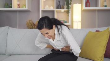 Woman suffering from severe abdominal pain. Woman sitting on sofa at home holds her belly and suffers holding her belly.
