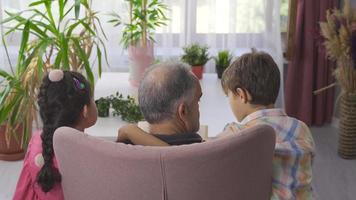 grand-père lisant des livres d'histoires à ses petits-enfants. les petits-enfants l'écoutent à côté de leur grand-père. video