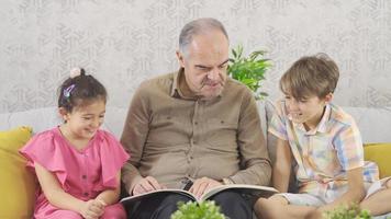 Grandfather and grandchildren are looking at the comic book. Grandparents and grandchildren who look at the comic are happy and sympathetic. video