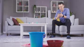 inundación. hombre mirando el agua que gotea del techo. gotea agua del techo del hombre que pide ayuda con su teléfono. video