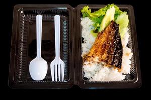 Parrilla pescado sobre arroz en caja de plástico, comida para llevar a casa foto