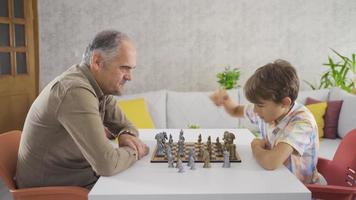 el abuelo está enseñando a su nieto. abuelo y nieto sentados en casa jugando al ajedrez. video