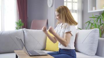 eccitato bellissimo donna vincitore sembra a il computer portatile celebra in linea successo si siede su divano a casa. ricevuto nuovo lontano attività commerciale opportunità, leggere bene notizia nel e-mail, gioito nel vittoria. video