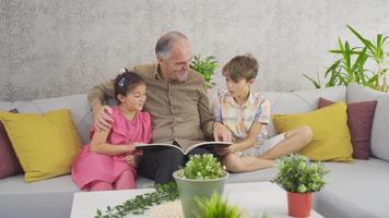 abuelo y nietos mirando el libro de revistas. anciano sentado en casa con sus nietos mirando libros de revistas. video