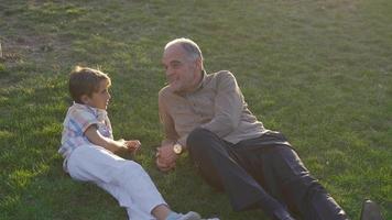 The old man and his grandson lying on the grass. The old man and the boy lying on the lawn are chatting. video