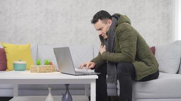 el hombre que trabaja con una computadora portátil tiene frío y frío en casa. hombre independiente frío en casa. video