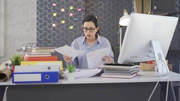 stressato e stanco attività commerciale donna Lavorando nel ufficio. giovane donna Lavorando a scrivania nel ufficio, guardare a documenti e computer, lavori e prende stanco e annoiato. video