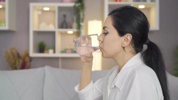 vrouw drinken water Bij huis. jong vrouw zittend Aan sofa Bij huis drinken water van glas. video
