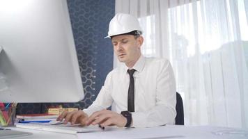 ingenieur, der in seinem büro mit computer arbeitet. der ingenieur im weißen helm arbeitet hart. video