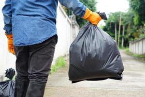 el hombre de primer plano sostiene una bolsa de plástico negra que contiene basura en su interior. concepto, gestión de residuos. problemas ambientales. tareas diarias. tirar basura. foto