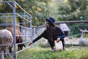 una mujer hermosa joven alimenta una oveja en el pueblo foto