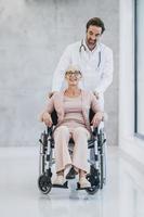 médico empujando a su paciente mayor en silla de ruedas por el pasillo del hospital foto