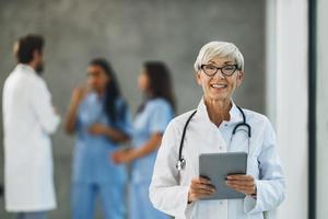 una doctora mirando la cámara mientras usa una tableta digital en el pasillo del hospital foto