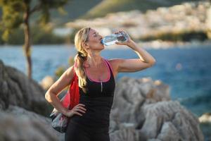 mujer corredora está bebiendo agua y tomando un descanso después de trotar cerca del mar foto