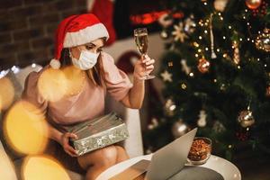 Woman Making Toast With Champagne And Holding Gift While Making Video Call On Christmas Eve At Home photo