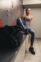 mujer descansando en el vestidor y sosteniendo una botella de agua después de un duro entrenamiento en el gimnasio foto