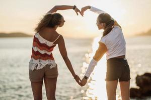 dos mujeres haciendo forma de corazón con las manos y disfrutando del atardecer en la playa foto