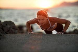 mujer practicando ejercicio push-up mientras trabaja al aire libre entrenando cerca del mar foto