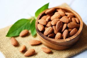 Almonds nuts on wooden bowl with leaf almonds top view on sack background - Roasted almond for snack photo