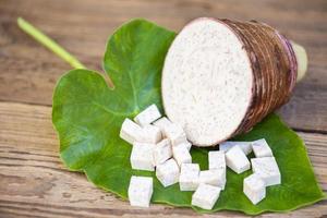 Taro root with half and slice cubes on taro leaf and wooden background, Fresh raw organic taro root ready to cook photo