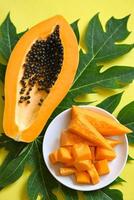 frutas de papaya sobre fondo amarillo, papaya madura fresca rebanada de fruta tropical con semilla de papaya y hojas de árbol de papaya foto