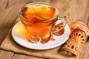 Bael tea on glass with dried bael slices on wooden background, Bael  juice - Dry bael fruit tea for health - Aegle marmelos photo