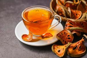 Bael tea on glass with dried bael slices on dark background, Bael  juice - Dry bael fruit tea for health - Aegle marmelos photo