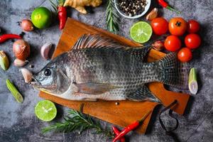 tilapia con especias romero tomate lima limón jengibre ajo pimienta chili sobre fondo oscuro, pescado tilapia crudo fresco de la granja de tilapia foto