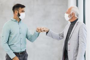 dos hombres de negocios saludando con los puños golpeados durante la pandemia del coronavirus en la oficina foto