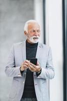 A Senior Business Man Using Smartphone While Standing Near The Window In The Office photo